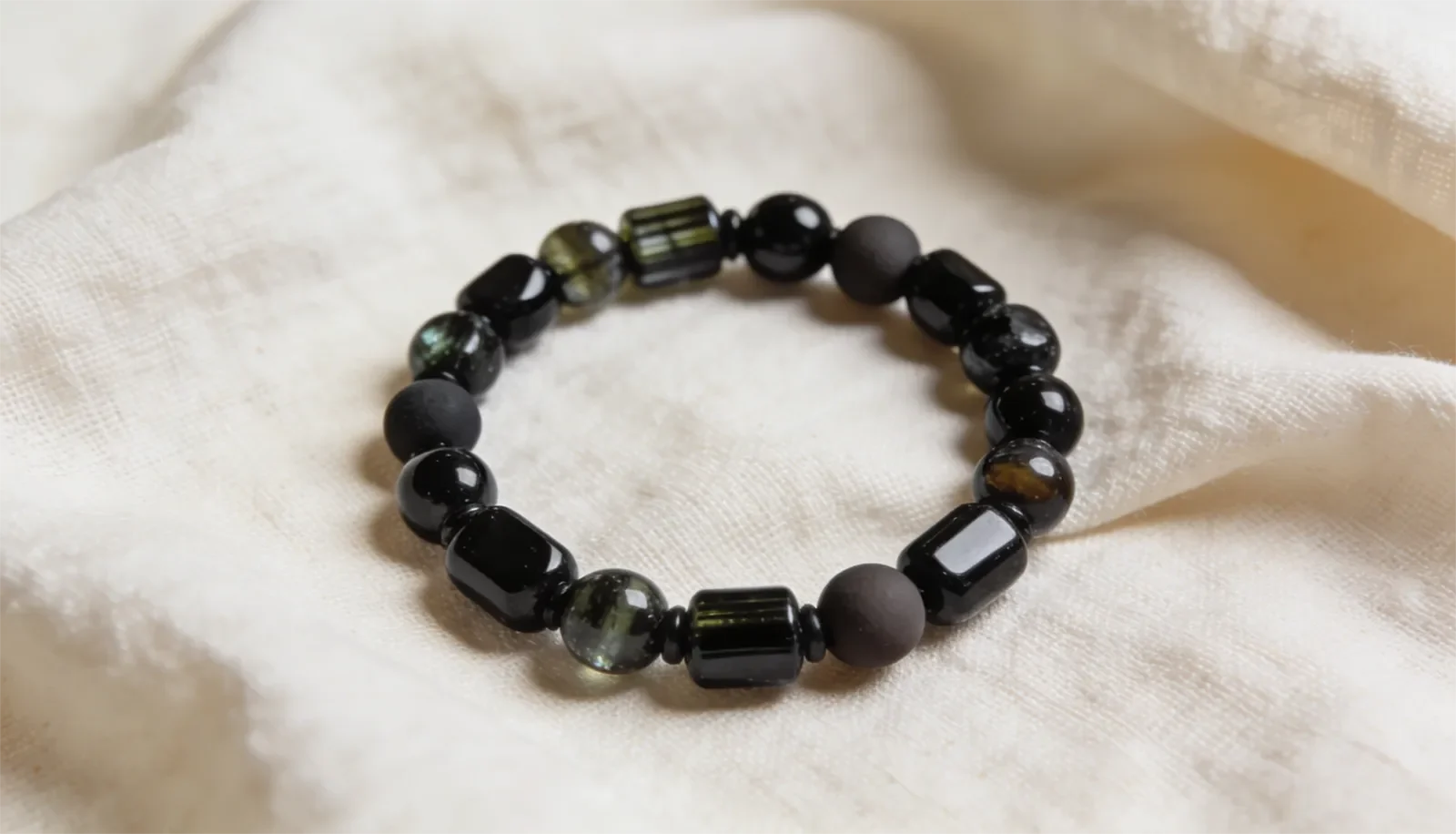 Vòng tay tourmaline đen hạt đen đặt trên nền vải màu kem sáng
