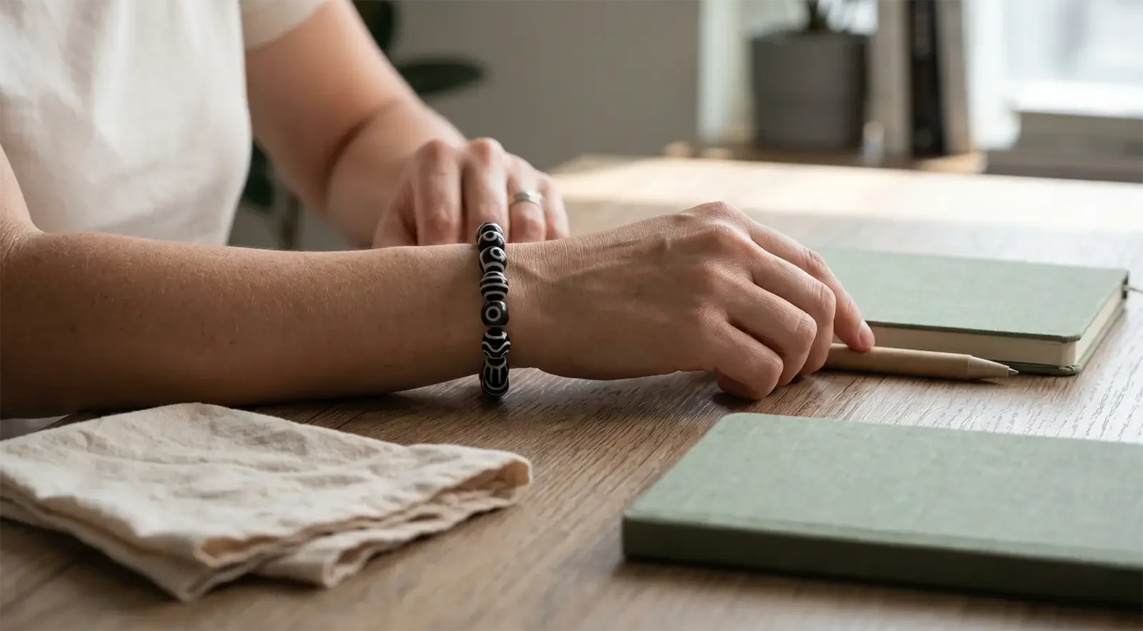 Vòng tay hạt Dzi đơn giản được đeo trong khoảnh khắc thường ngày yên tĩnh bên bàn gỗ, sổ tay và khăn mềm